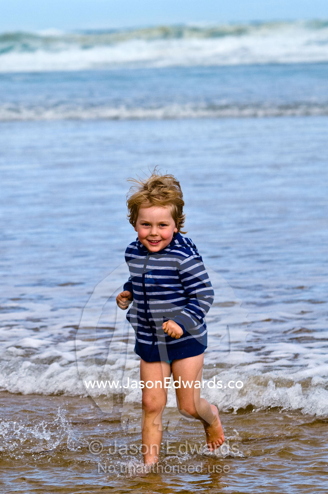 A fit and energetic blonde boy runs into the waves at the beach. Venus Bay, Bass Strait, South Gippsland, Victoria, Australia.