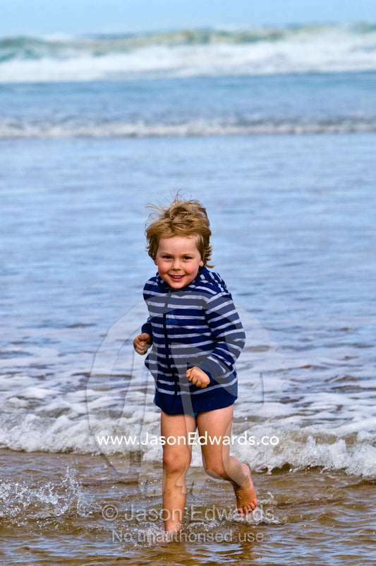 A fit and energetic blonde boy runs into the waves at the beach. Venus Bay, Bass Strait, South Gippsland, Victoria, Australia.