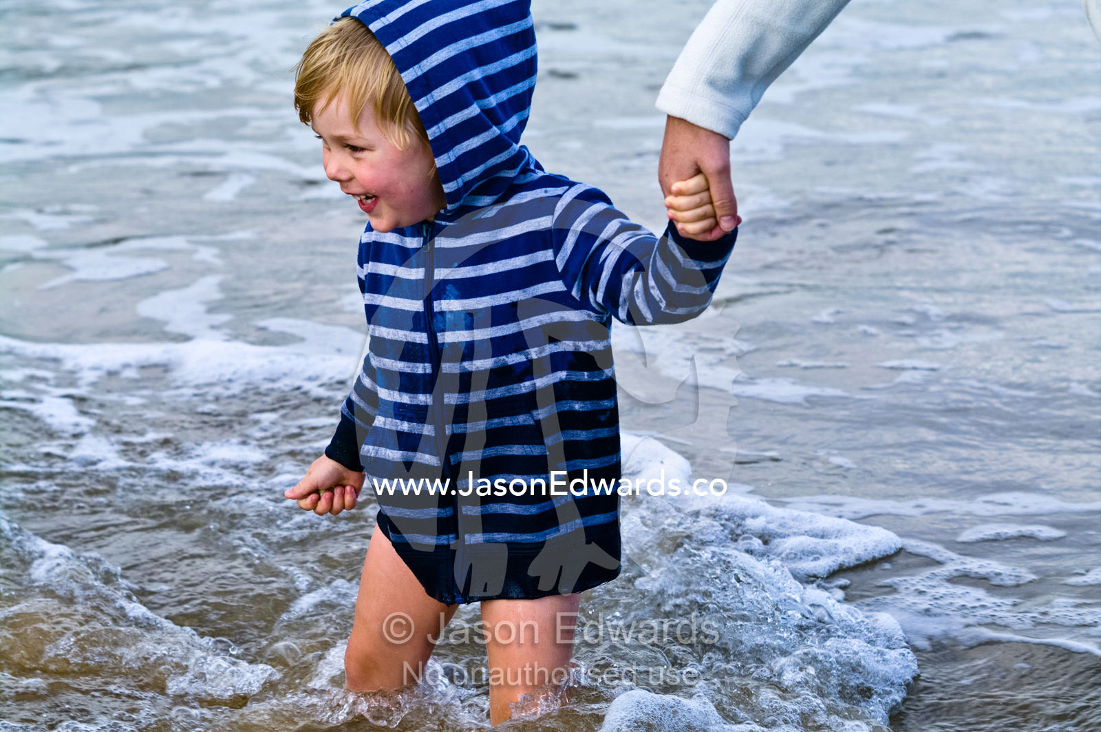 An excited and happy boy walks in the waves holding his mum's hand. Venus Bay, Bass Strait, South Gippsland, Victoria, Australia.