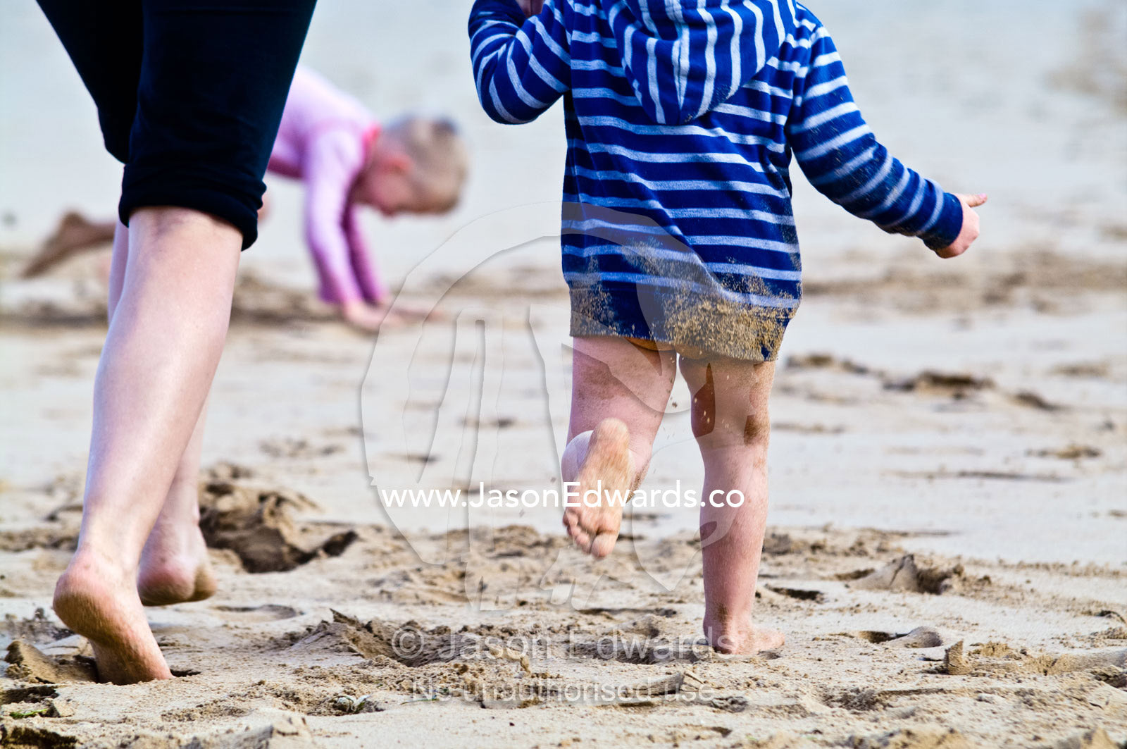 A small boy covered in wet sand running on the beach with his mum. Venus Bay, Bass Strait, South Gippsland, Victoria, Australia.
