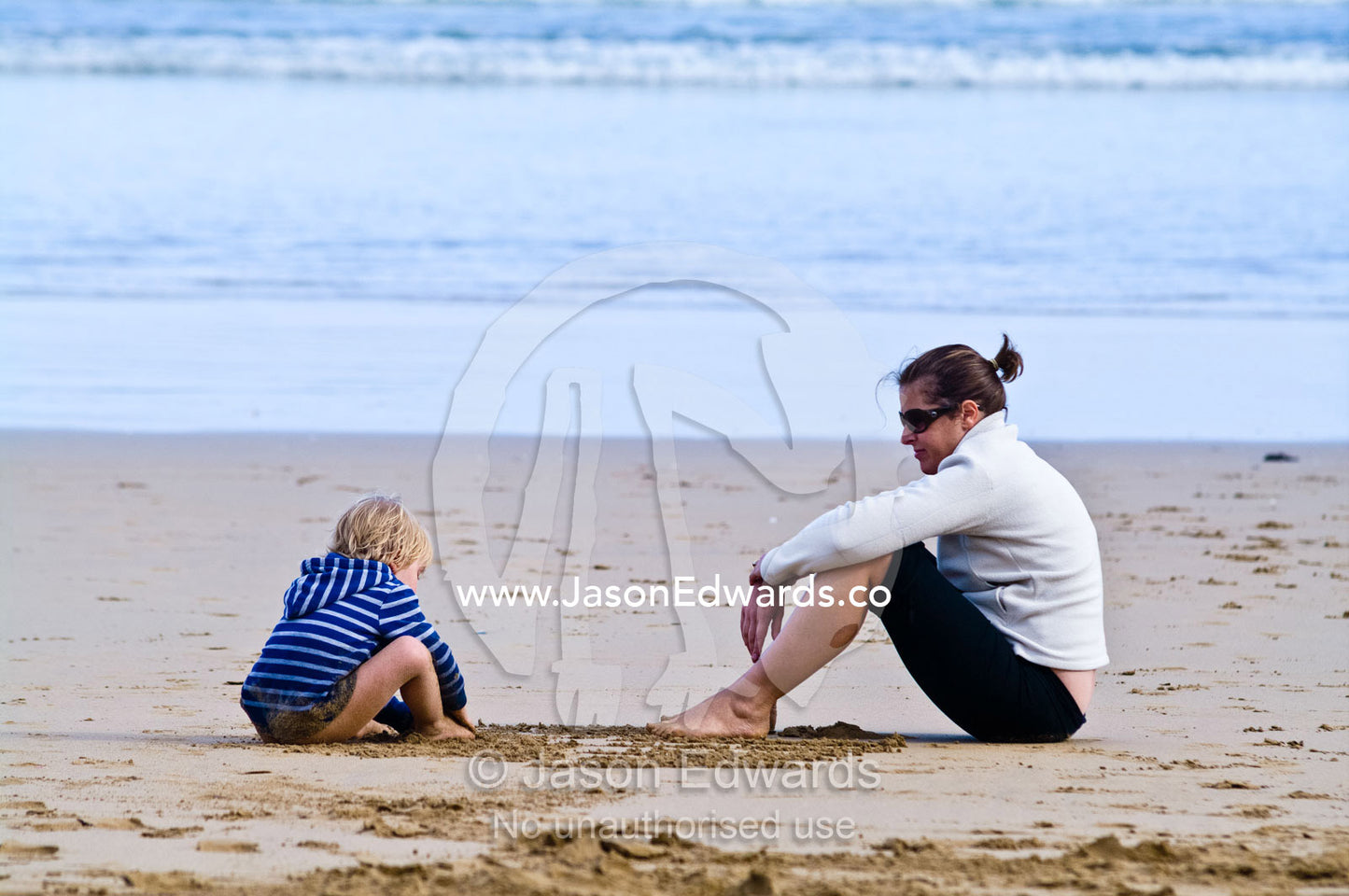 A boy and his mother draw patterns in the sand on the beach. Venus Bay, Bass Strait, South Gippsland, Victoria, Australia.
