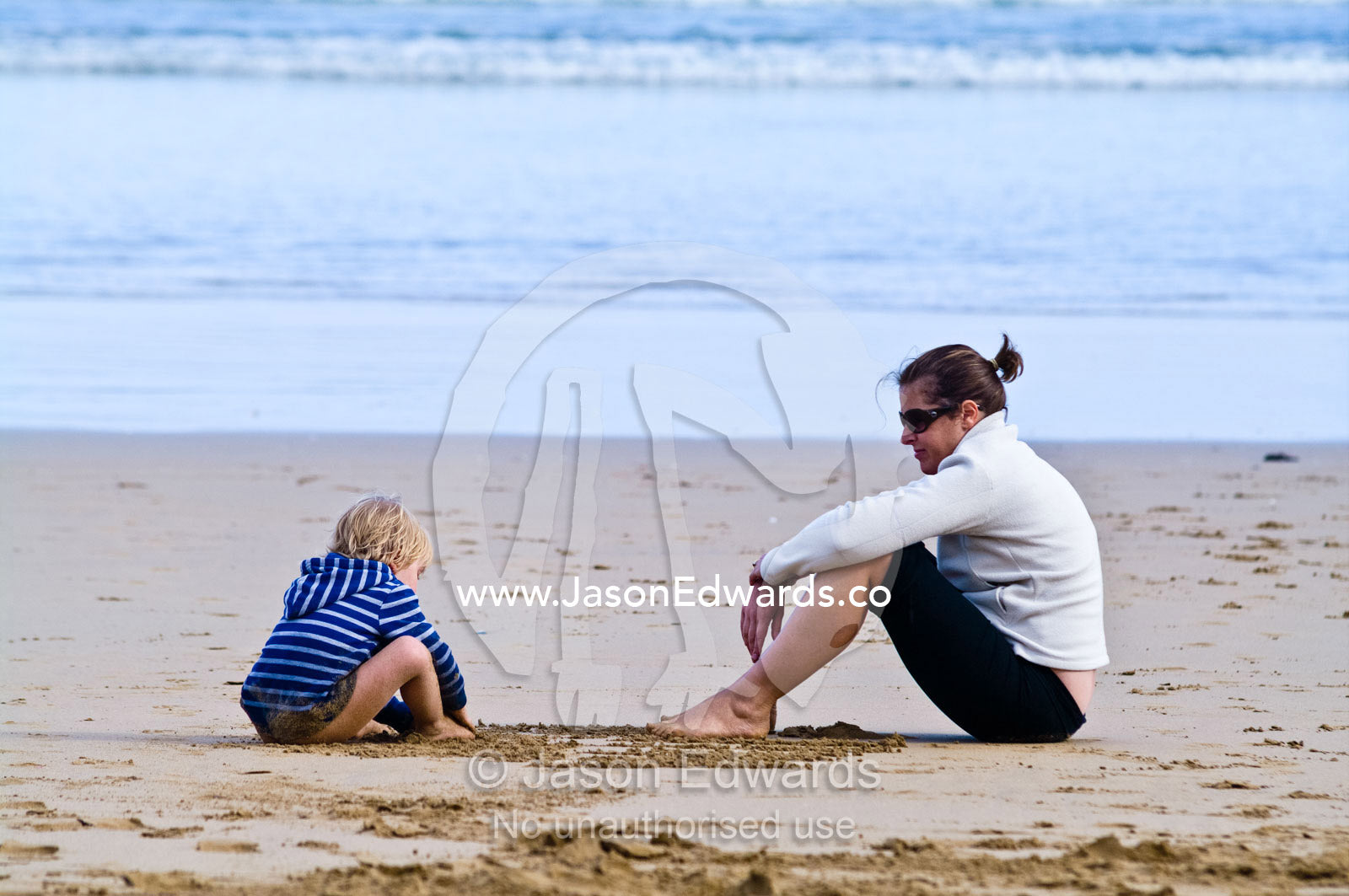 A boy and his mother draw patterns in the sand on the beach. Venus Bay, Bass Strait, South Gippsland, Victoria, Australia.