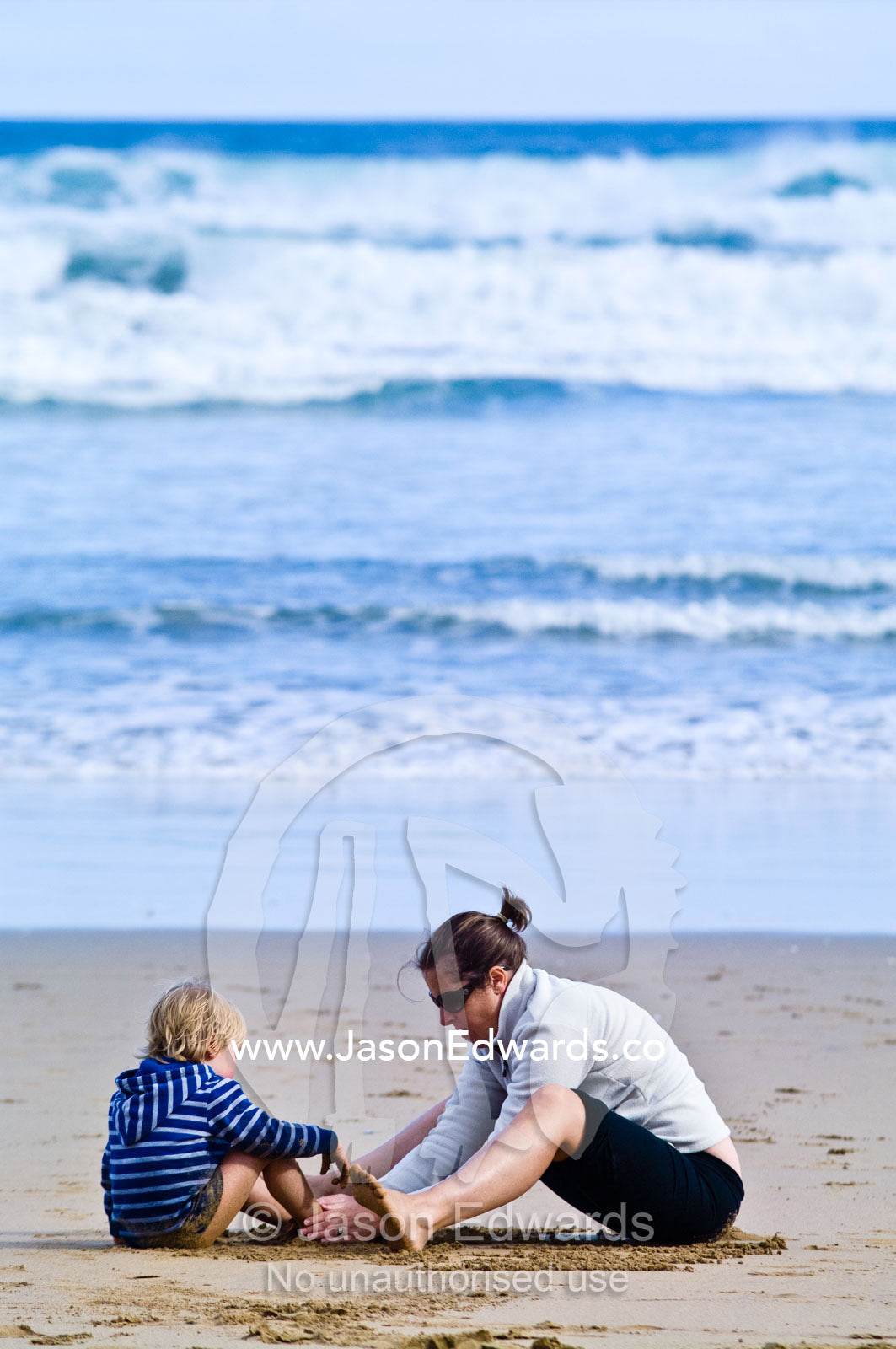 A boy and his mother draw patterns in the sand on the beach. Venus Bay, Bass Strait, South Gippsland, Victoria, Australia