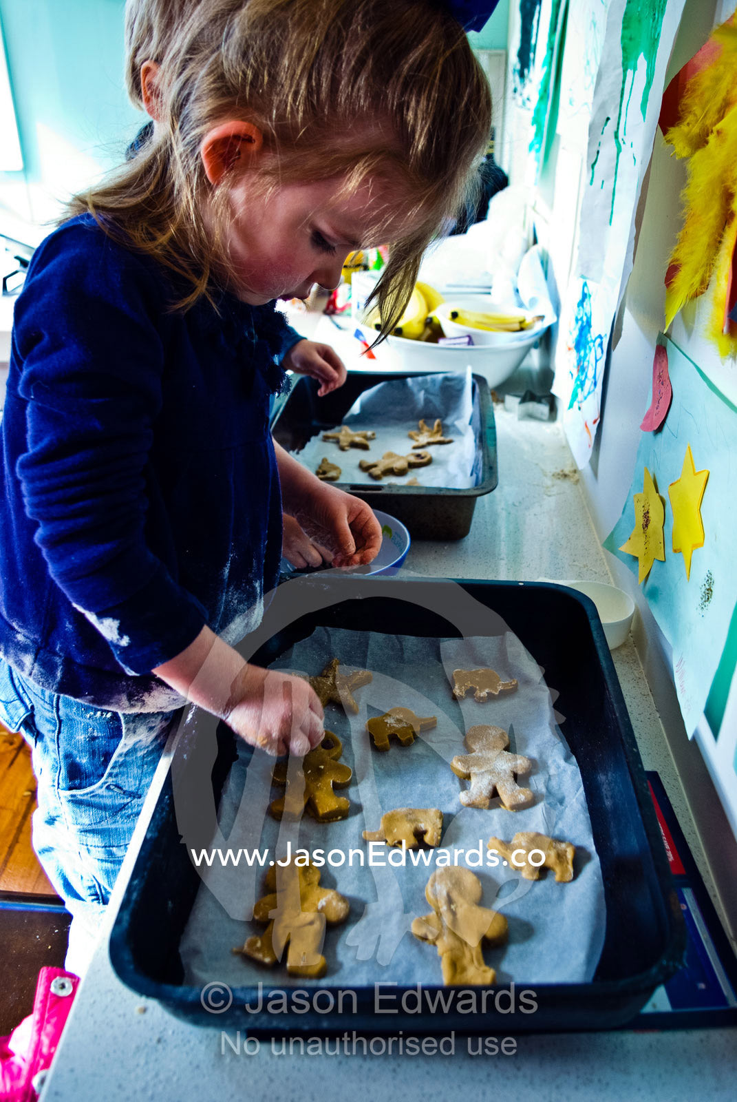 A young girl attaches eyes and buttons to her gingerbread men to bake. Carlton North, Melbourne, Victoria, Australia.