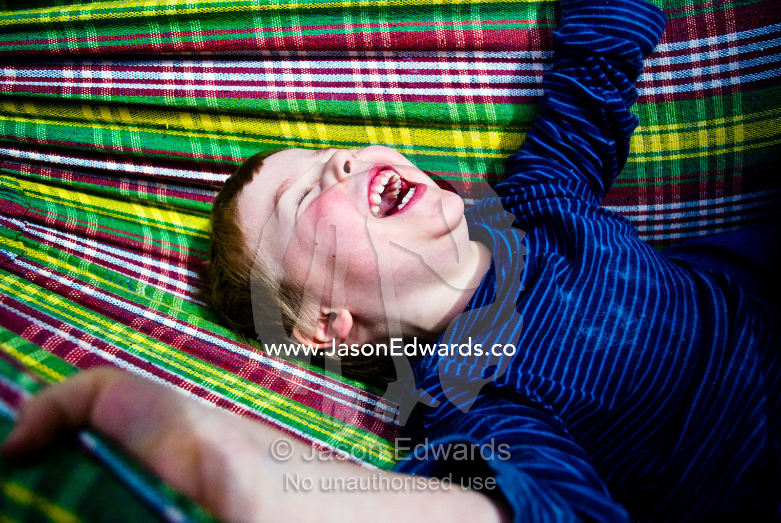 A young boy laughing hysterically whilst swinging in a tartan hammock. Carlton North, Melbourne, Victoria, Australia.