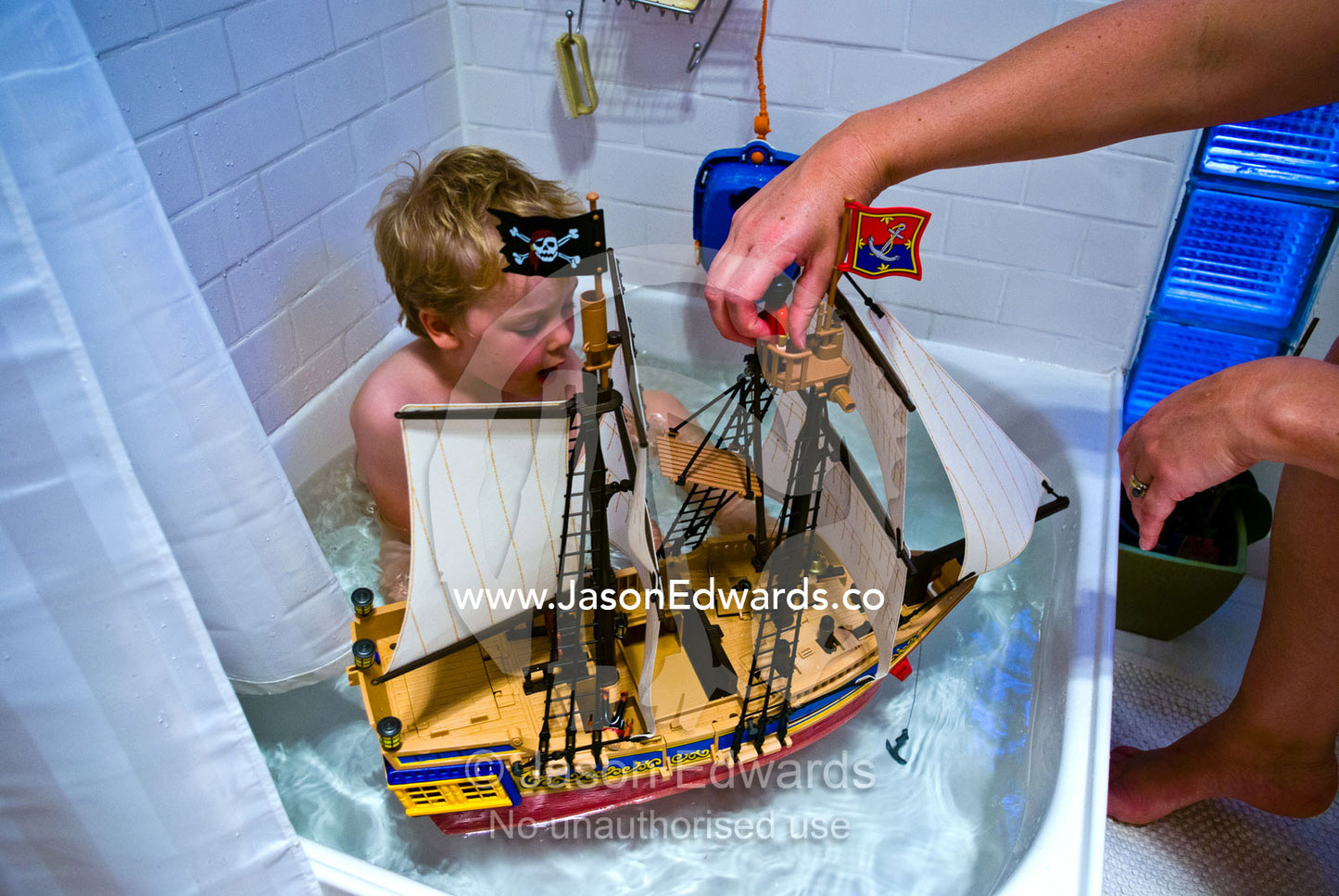 A boy and his mother play with a plastic toy pirate ship in the bath. Carlton North, Melbourne, Victoria, Australia.