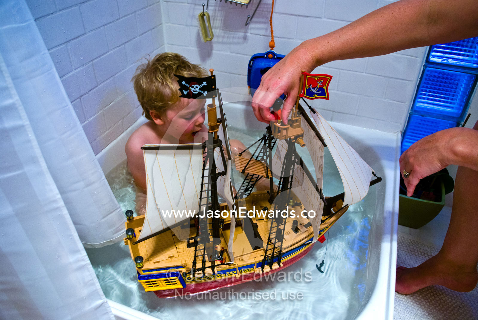 A boy and his mother play with a plastic toy pirate ship in the bath. Carlton North, Melbourne, Victoria, Australia.