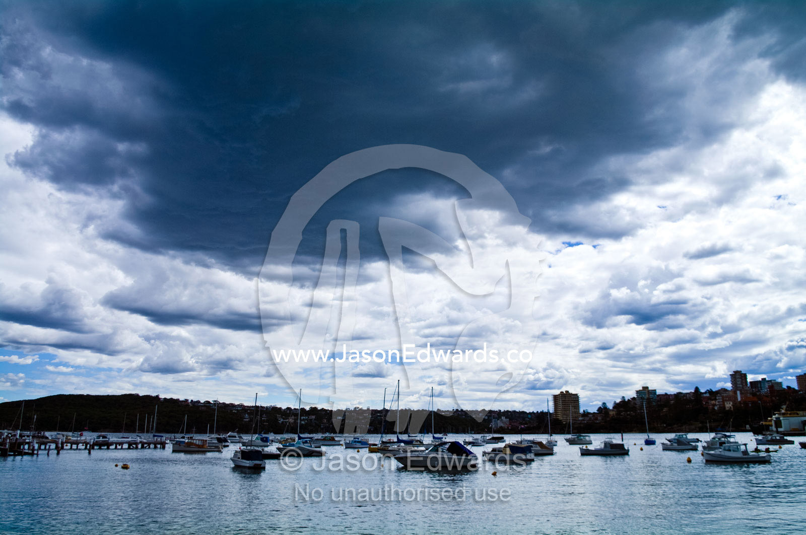 Dark, grey summer storm clouds descend over boats in a sheltered bay. East Esplanade Park, Manly Cove, Manly, Sydney Harbour, Sydney, New South Wales, Australia.