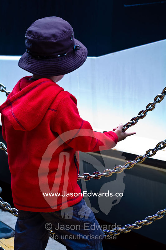 A young boy waits behind a chain fence to board a Sydney Harbour ferry Sydney Harbour, Sydney Cove, Warrane, Port Jackson, Circular Quay, Sydney, New South Wales, Australia.