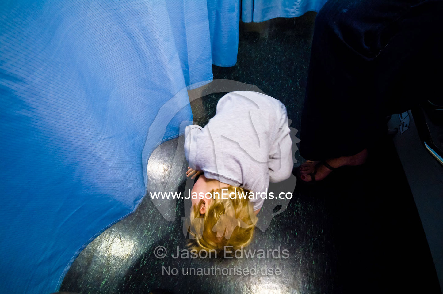 A boy awaiting surgery in a hospital looks under a surgical curtain. Epworth Freemasons Hospital, East Melbourne, Victoria, Australia.
