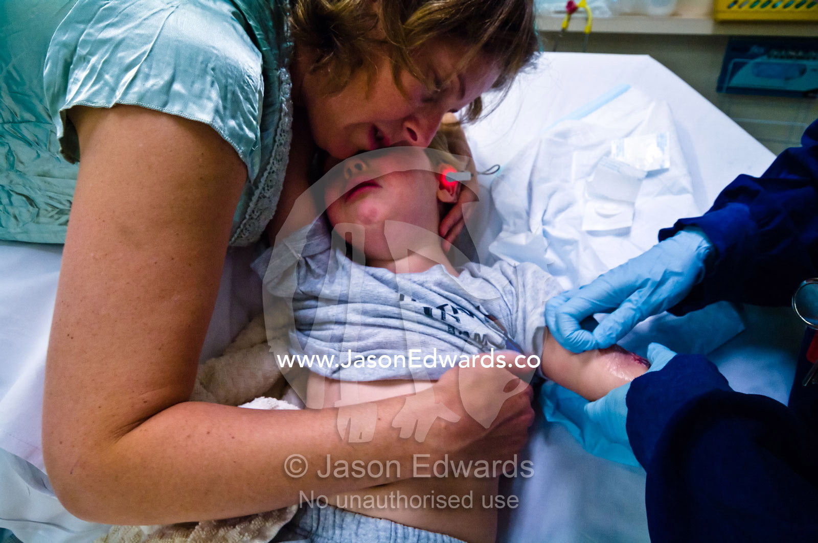 A mother comforts a distressed son as a doctor removes a saline drip. Epworth Freemasons Hospital, East Melbourne, Victoria, Australia.