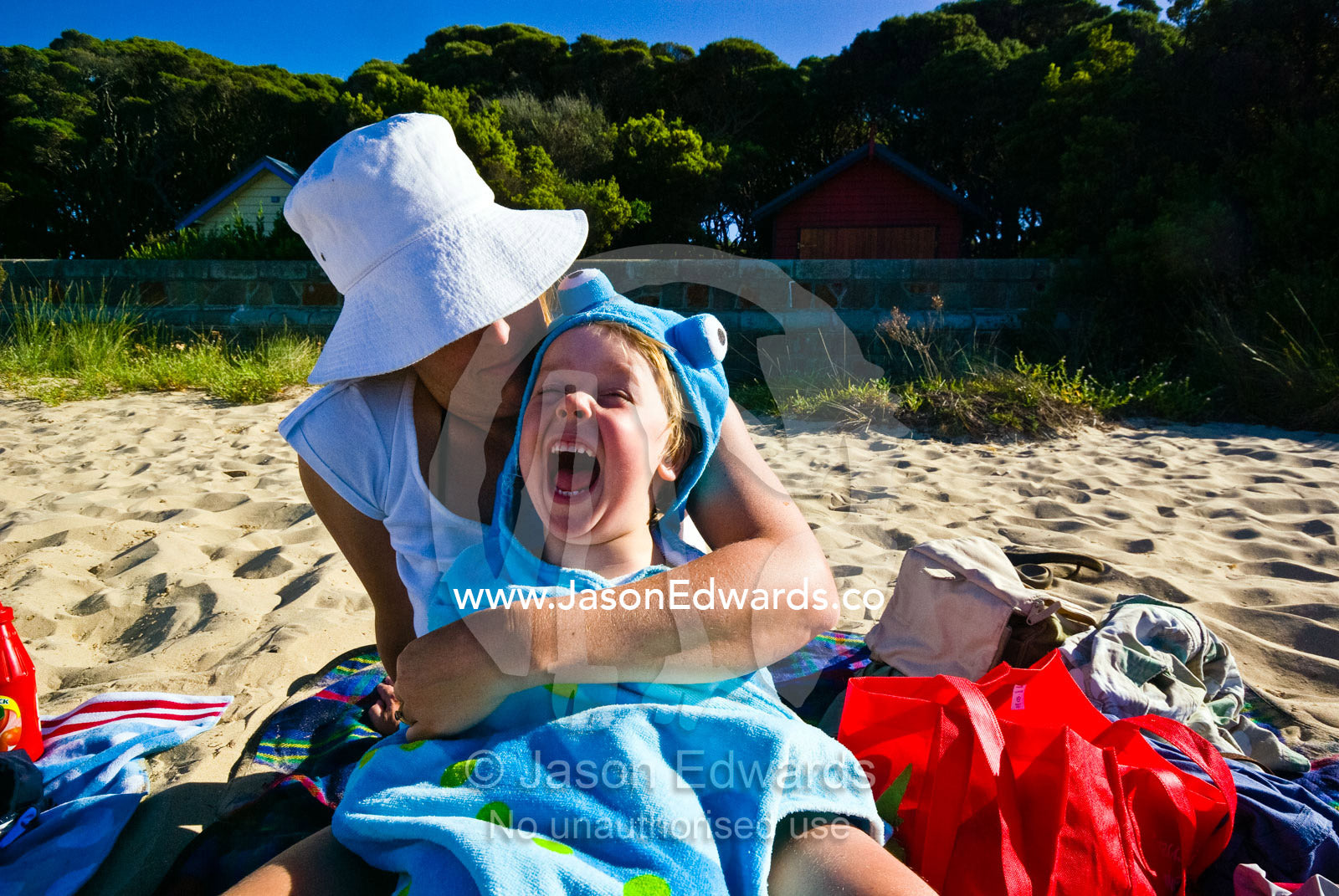 A mother cuddles her laughing son on the beach during summer holidays. Rye Beach, Melbourne, Victoria, Australia.