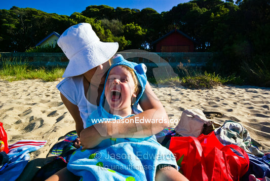 A mother cuddles her laughing son on the beach during summer holidays. Rye Beach, Melbourne, Victoria, Australia.