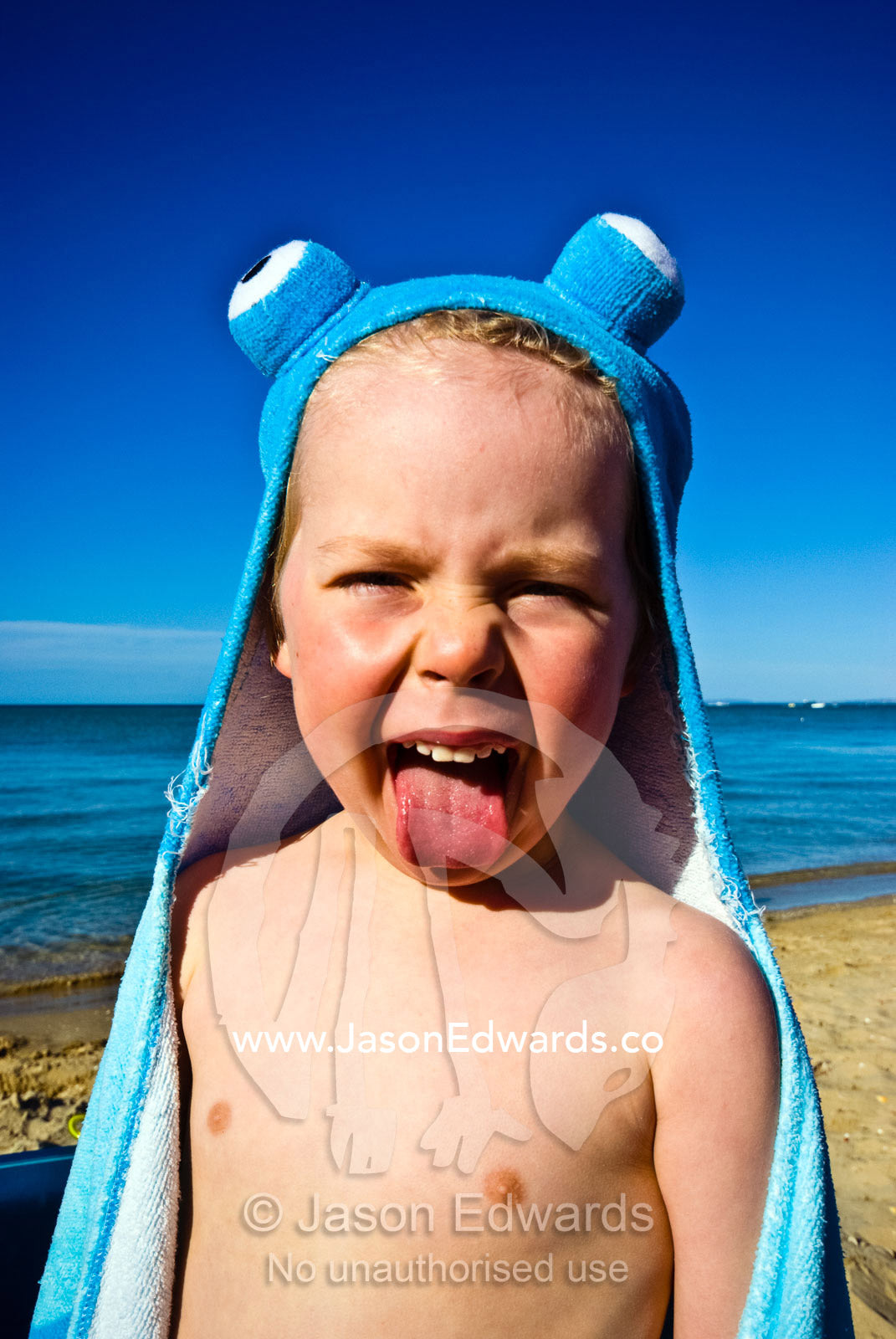 A cheeky boy pokes out his tongue whilst wrapped in an octopus towel. Rye Beach, Melbourne, Victoria, Australia.