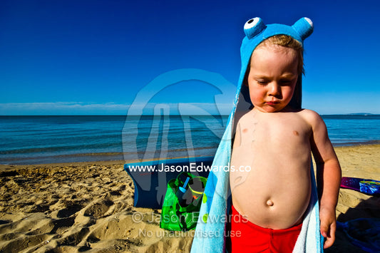 A cheeky boy pokes out his tummy whilst wrapped in an octopus towel. Rye Beach, Melbourne, Victoria, Australia.