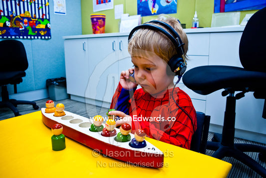 A boy undergoes a clinical hearing test using headphones and toys. Carlton, Melbourne, Victoria, Australia.