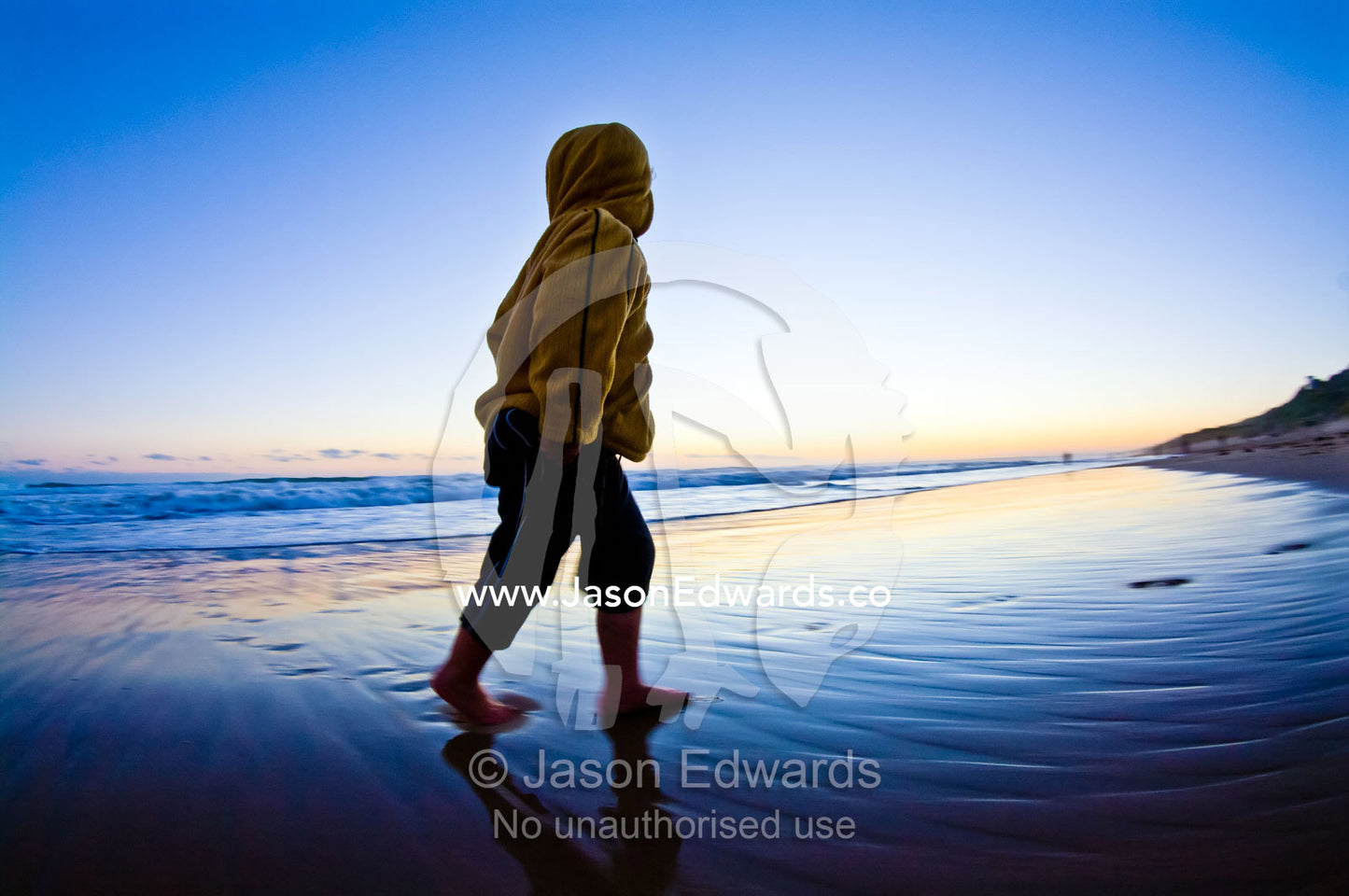 A small boy runs from waves on a remote stretch of beach at twilight. Venus Bay, Cape Liptrap Coastal Park, Bass Strait, South Gippsland, Victoria, Australia.