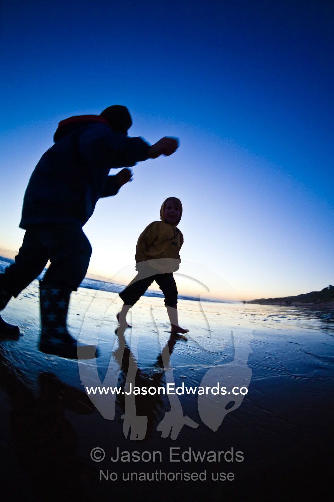 Small boys run from waves on a remote stretch of beach at twilight. Venus Bay, Cape Liptrap Coastal Park, Bass Strait, South Gippsland, Victoria, Australia.