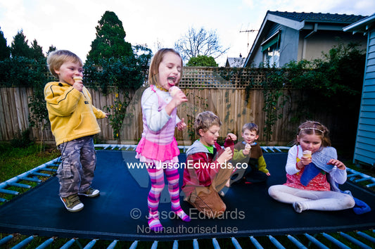 Cousins and friends playing on a trampoline whilst eating ice-cream. Malvern East, Melbourne, Victoria, Australia.