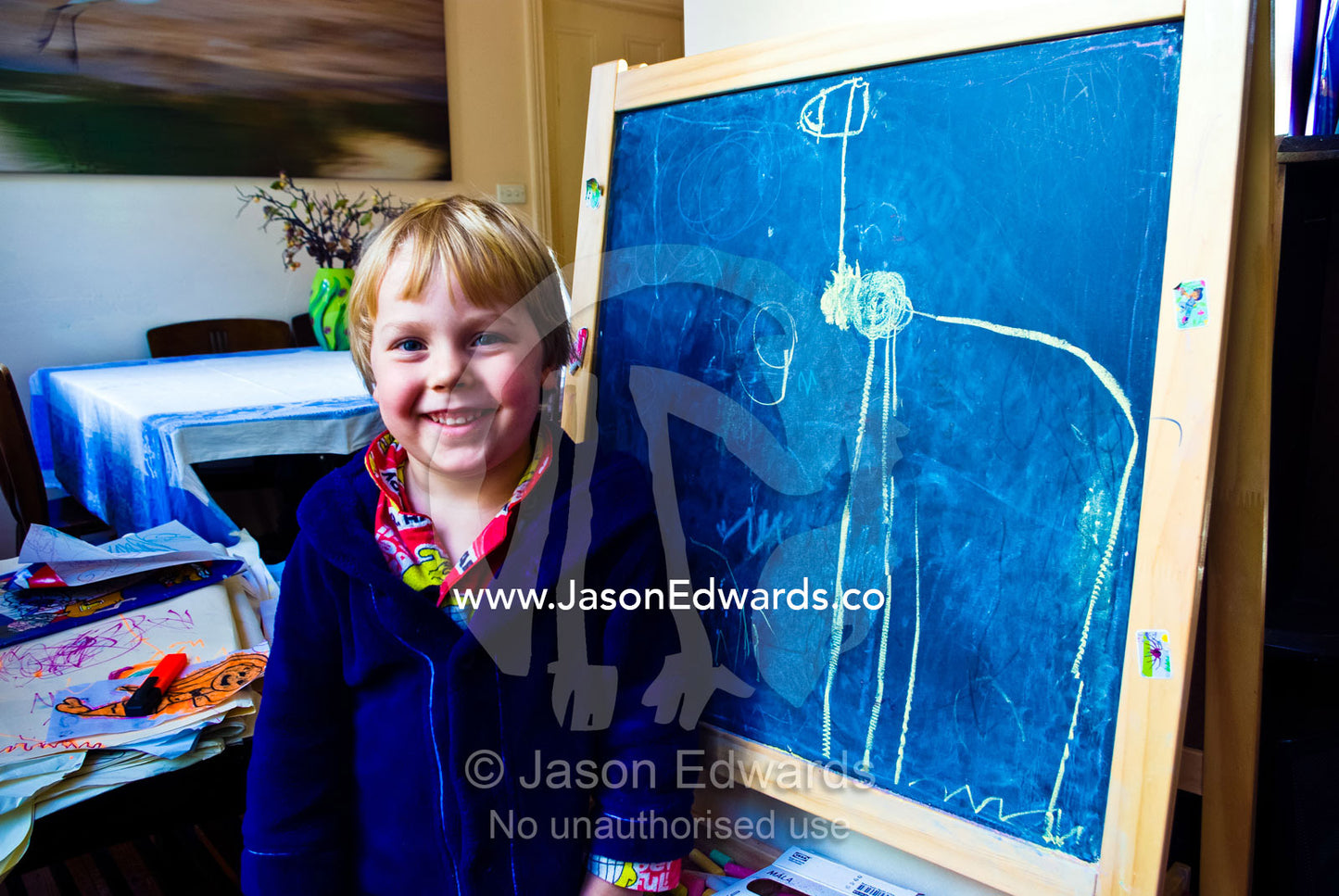 A boys stands proudly next to his chalkboard drawing of a giraffe. Carlton North, Melbourne, Victoria, Australia.