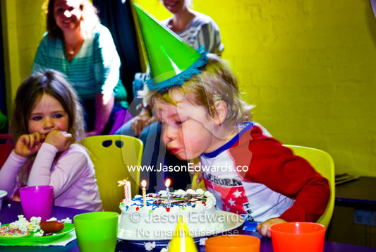 A boy blows out candles on his cake at his fourth birthday party. Hawthorn, Melbourne, Victoria, Australia.