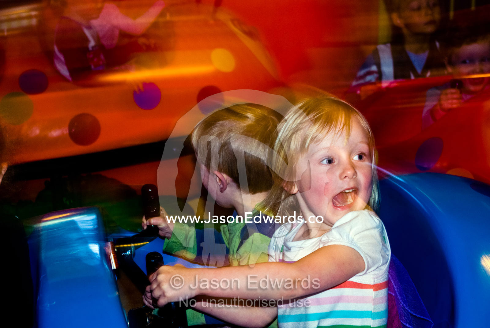 A sister and brother scream for joy on a beetle ride at a play centre. Hawthorn, Melbourne, Victoria, Australia.