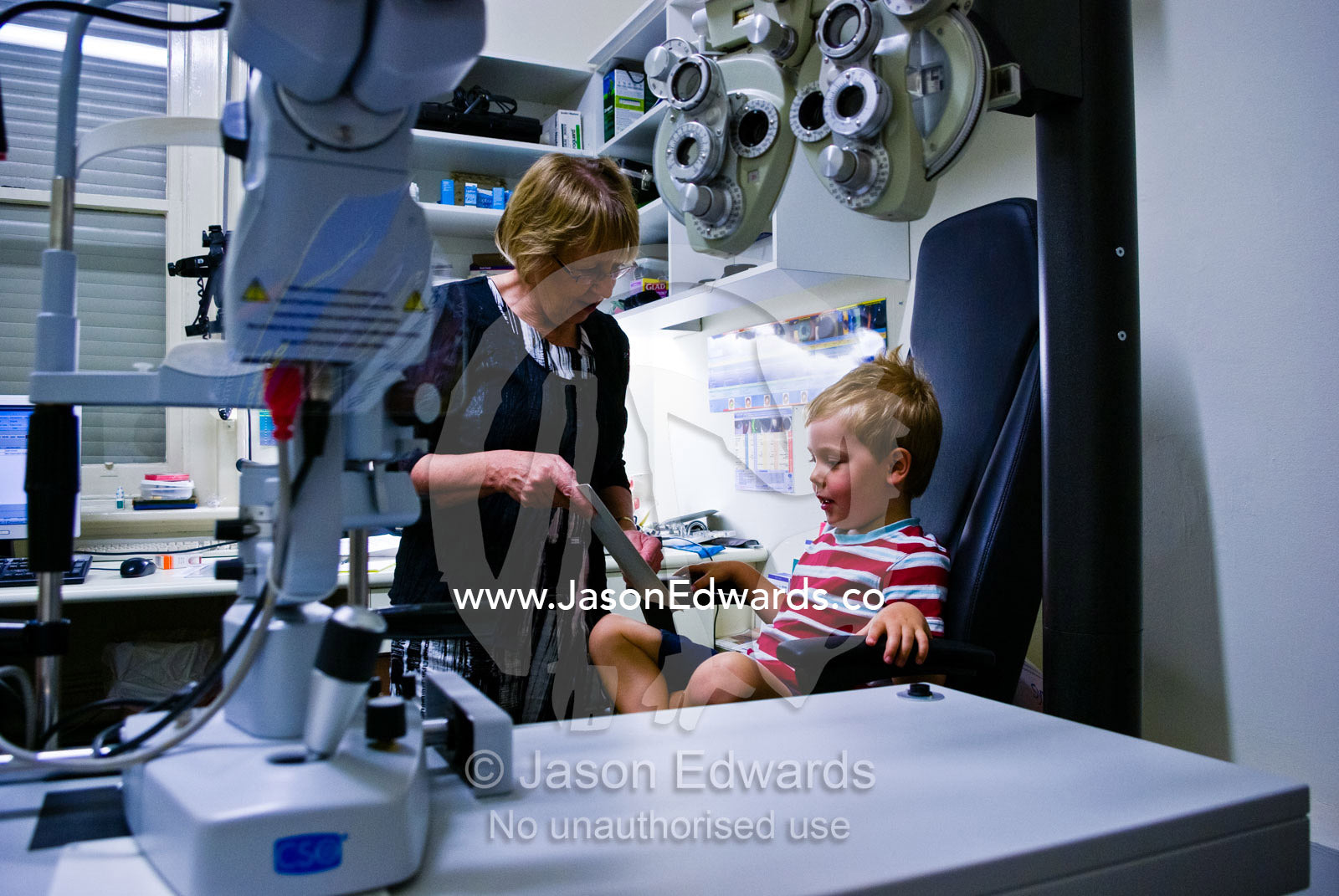 An optometrist gives a small boy his first eye chart examination. Hawthorn, Melbourne, Victoria, Australia.
