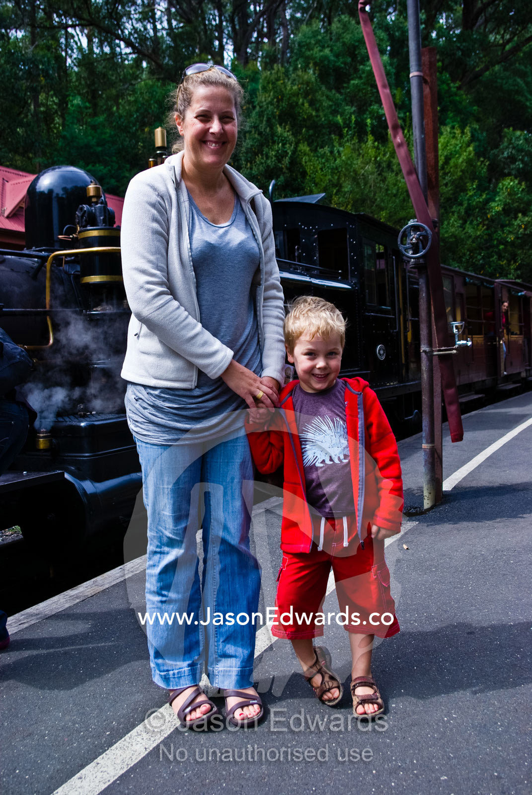 A mother and son wait to board an antique steam train in the forest. Lakeside, Emerald, Melbourne, Victoria, Australia.