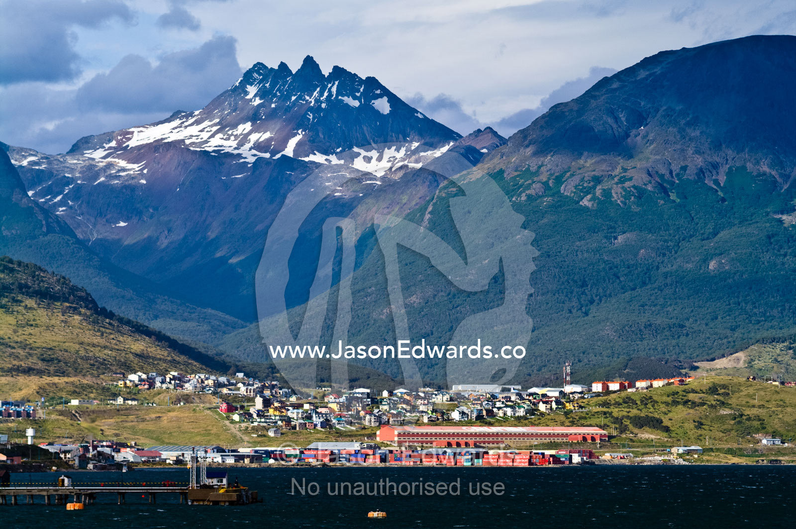 Shipping containers and warehouses line a port beneath an alpine city. Ushuaia, Martial Mountains, Fuegian Andes, Ushuaia Bay, The Beagle Channel, Tierra del Fuego Archipelago, Straits of Magellan, Tierra del Fuego Province, Patagonia, Argentina.