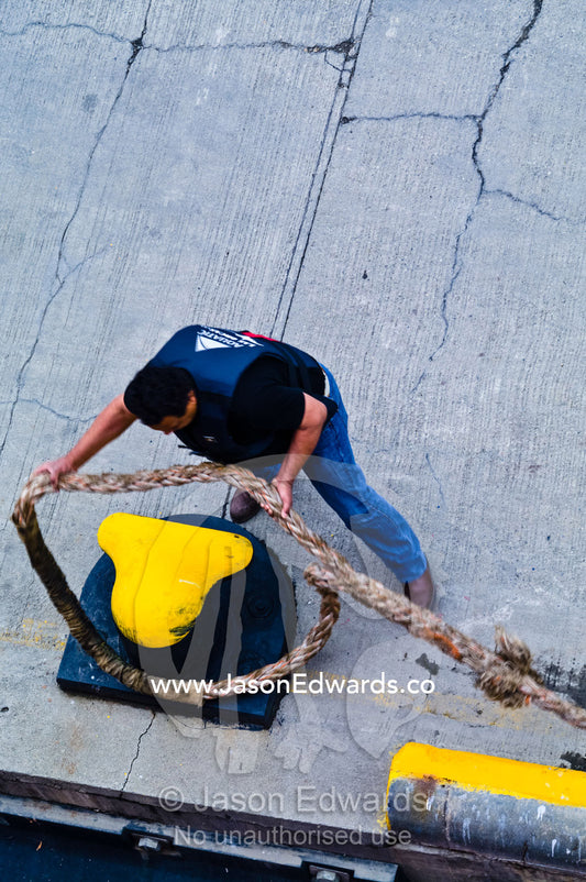 A wharf worker unhooks a ships mooring rope from a pier bollard. Ushuaia, Martial Mountains, Fuegian Andes, Ushuaia Bay, The Beagle Channel, Tierra del Fuego Archipelago, Straits of Magellan, Tierra del Fuego Province, Patagonia, Argentina.