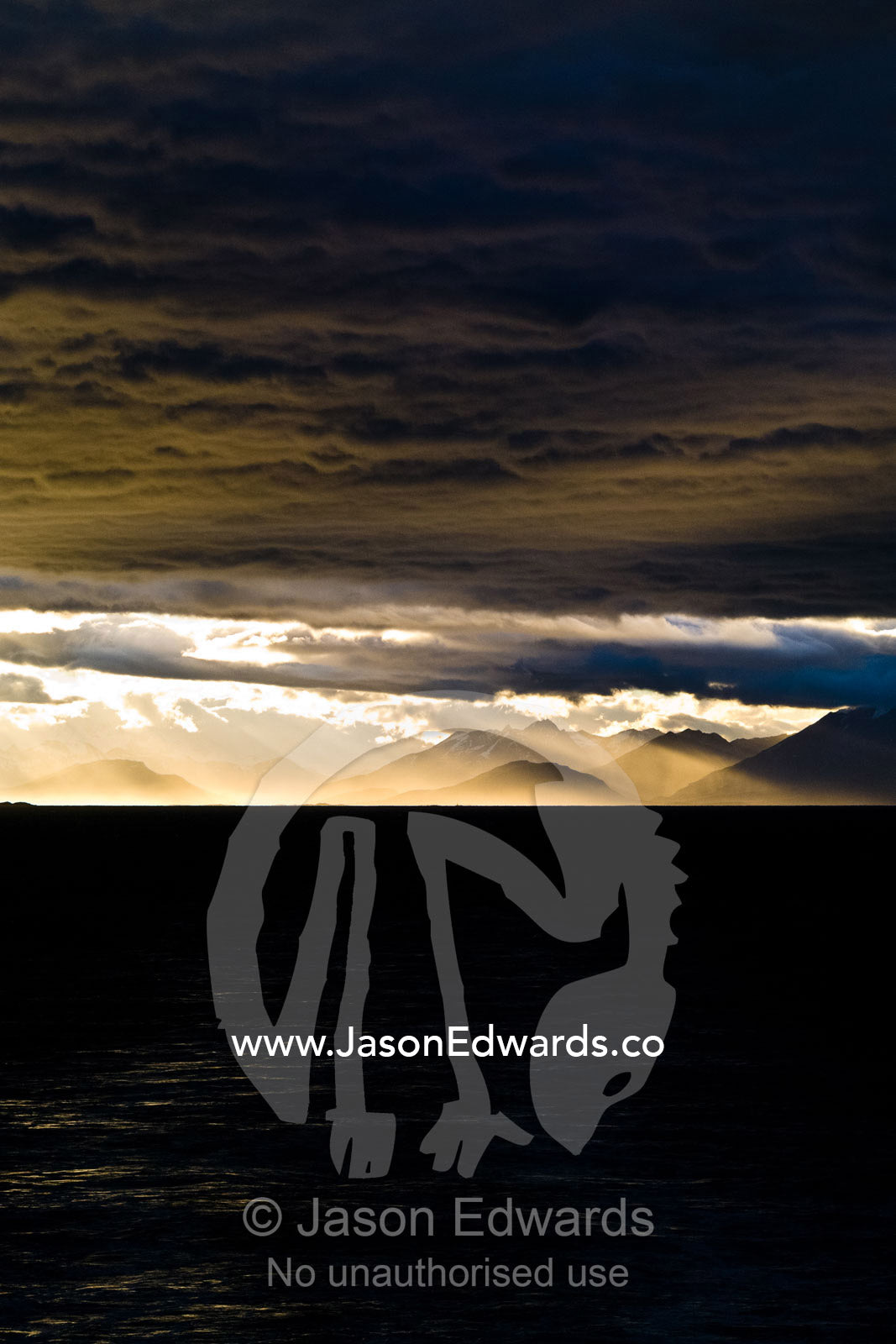 A sunset storm over the Andes turns sea mist and clouds golden. Ushuaia, Martial Mountains, Fuegian Andes, Ushuaia Bay, The Beagle Channel, Tierra del Fuego Archipelago, Straits of Magellan, Tierra del Fuego Province, Patagonia, Argentina.