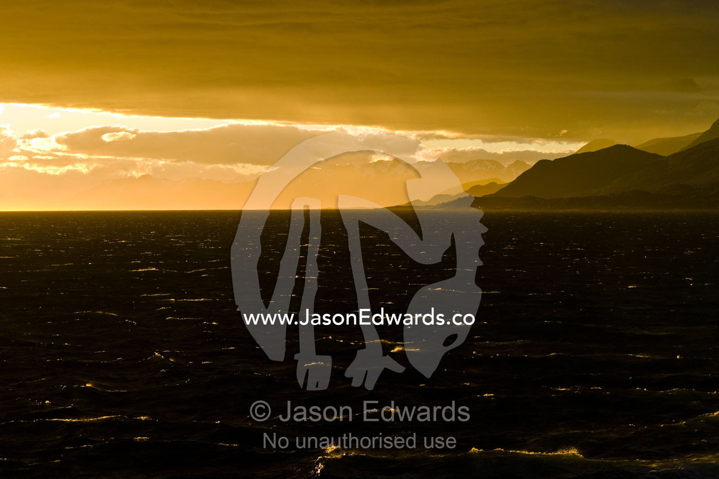The setting sun turns whitecaps on a windy ocean surface golden. Ushuaia, Martial Mountains, Fuegian Andes, Ushuaia Bay, The Beagle Channel, Tierra del Fuego Archipelago, Straits of Magellan, Tierra del Fuego Province, Patagonia, Argentina.