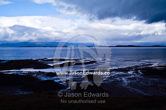 An icy rugged and rocky shoreline beneath storm clouds at low tide. Ushuaia Bay, The Beagle Channel, Tierra del Fuego Archipelago, Straits of Magellan, Ushuaia, Tierra del Fuego Province, Patagonia, Argentina.
