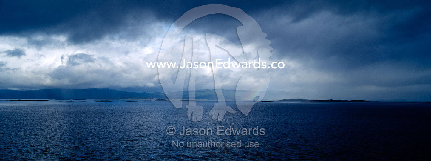 A rainbow descends from a storm front and rainstorm over an ocean bay. Ushuaia Bay, The Beagle Channel, Tierra del Fuego Archipelago, Straits of Magellan, Ushuaia, Tierra del Fuego Province, Patagonia, Argentina.