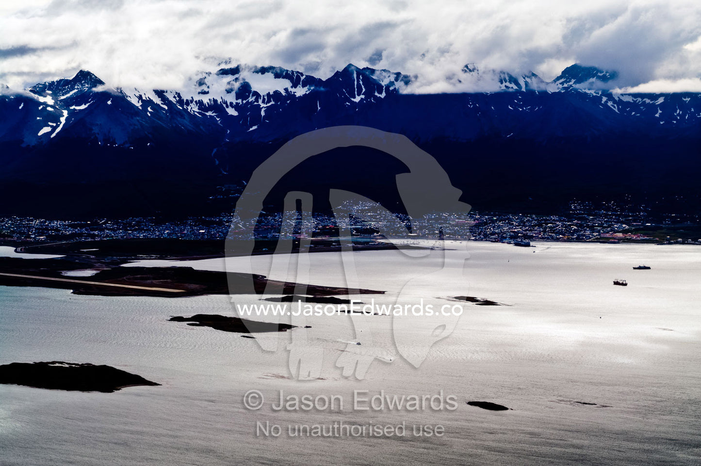 Storm clouds descend over the Andes Mountains above a sprawling city. Ushuaia Bay, The Beagle Channel, Fuegian Andes, Tierra del Fuego Archipelago, Straits of Magellan, Ushuaia, Tierra del Fuego Province, Patagonia, Argentina.