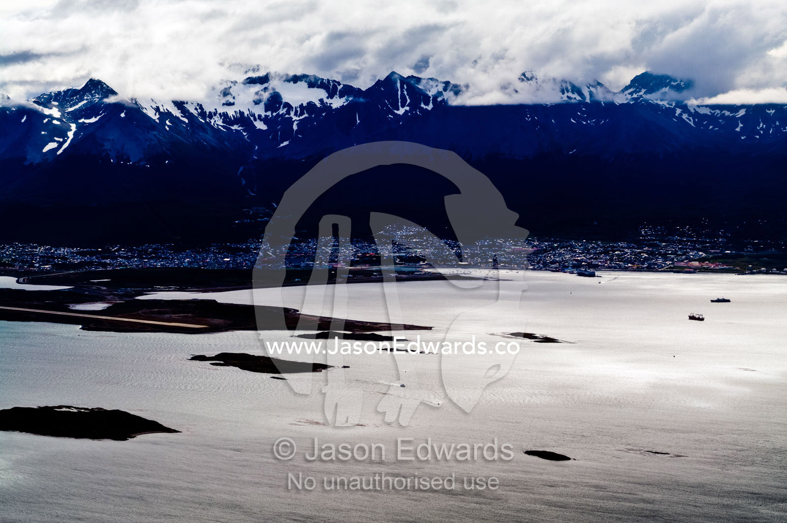 Storm clouds descend over the Andes Mountains above a sprawling city. Ushuaia Bay, The Beagle Channel, Fuegian Andes, Tierra del Fuego Archipelago, Straits of Magellan, Ushuaia, Tierra del Fuego Province, Patagonia, Argentina.