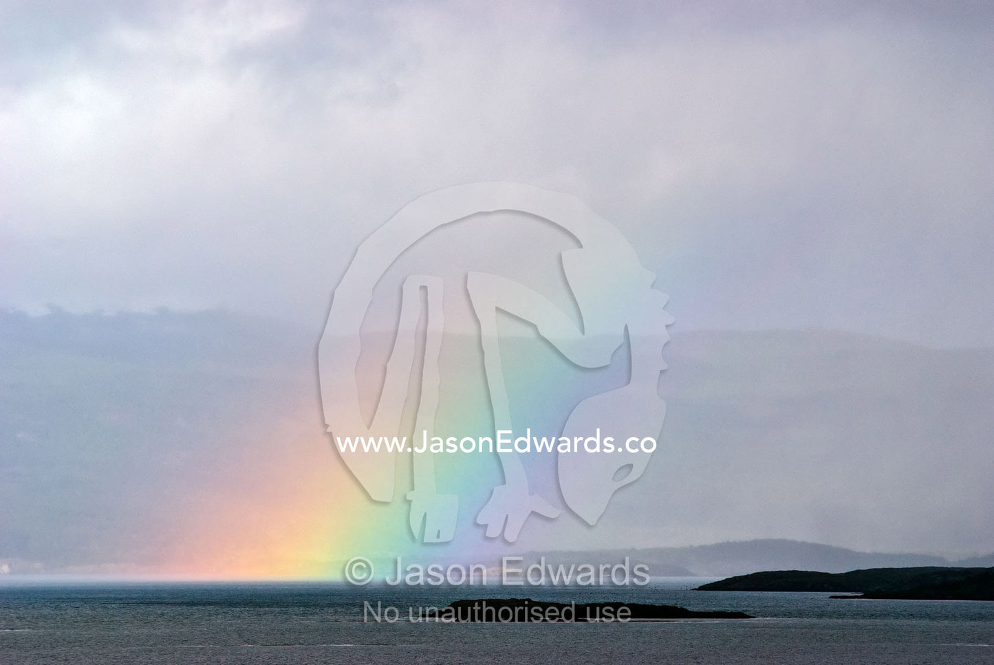 A rainbow rises from the ocean surface above a small rocky island. Ushuaia Bay, Chilean Andes, Fuegian Andes, The Beagle Channel, Tierra del Fuego Archipelago, Straits of Magellan, Ushuaia, Tierra del Fuego Province, Patagonia, Argentina.