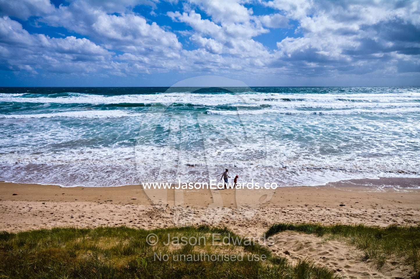 A mother and son play in the waves on a wide stormy beach in summer. Venus Bay, Cape Liptrap Coastal Park, Bass Strait, South Gippsland, Victoria, Australia.