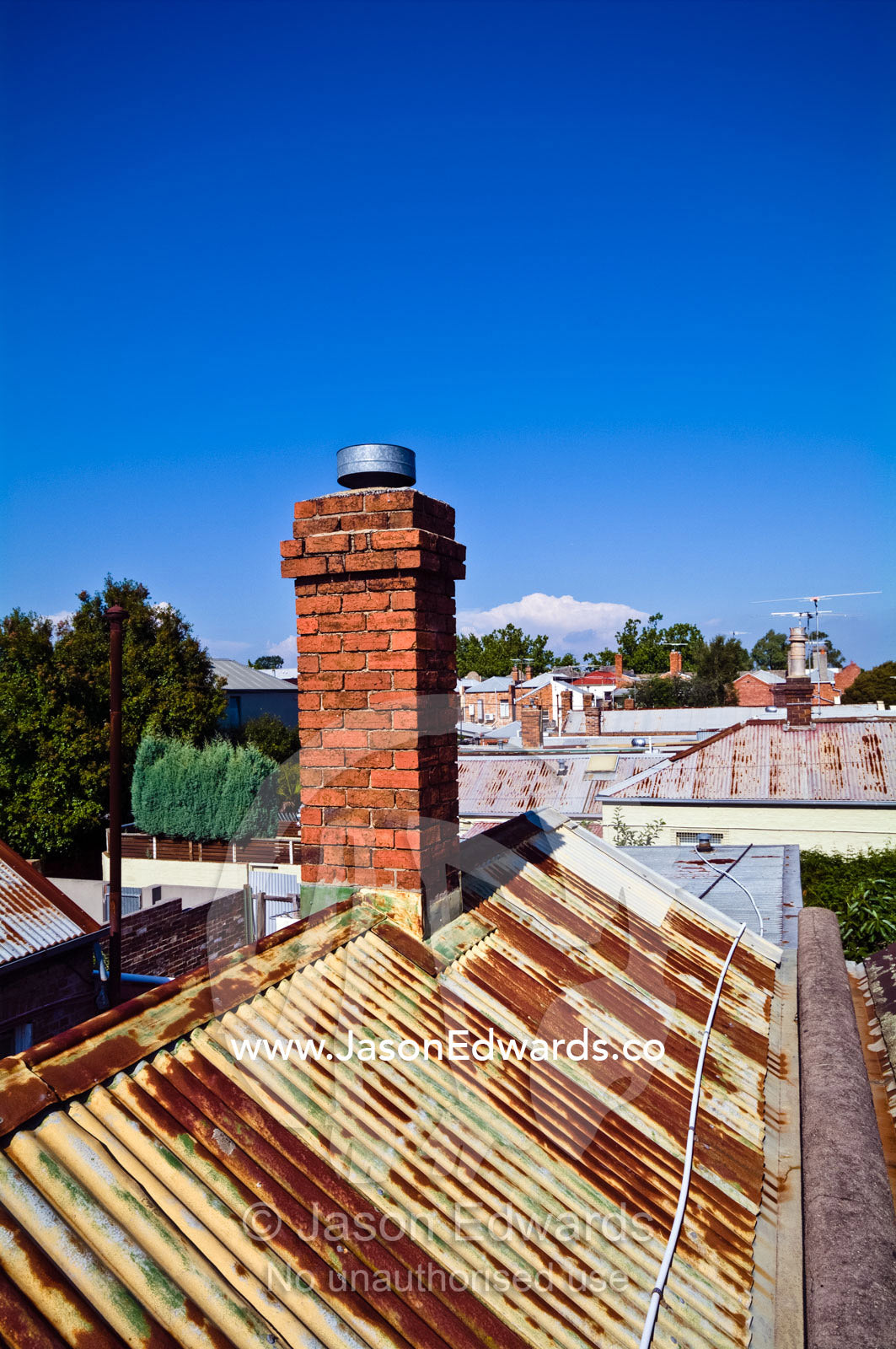 A Victorian red brick chimney pitched on a rusty corrugated iron roof. Carlton North, Melbourne, Victoria, Australia.
