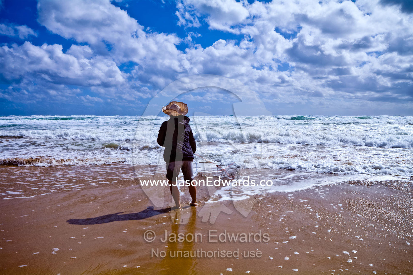 A woman fishes for pipi using a fishing line and basket in the surf. Venus Bay, Cape Liptrap Coastal Park, Bass Strait, South Gippsland, Victoria, Australia.