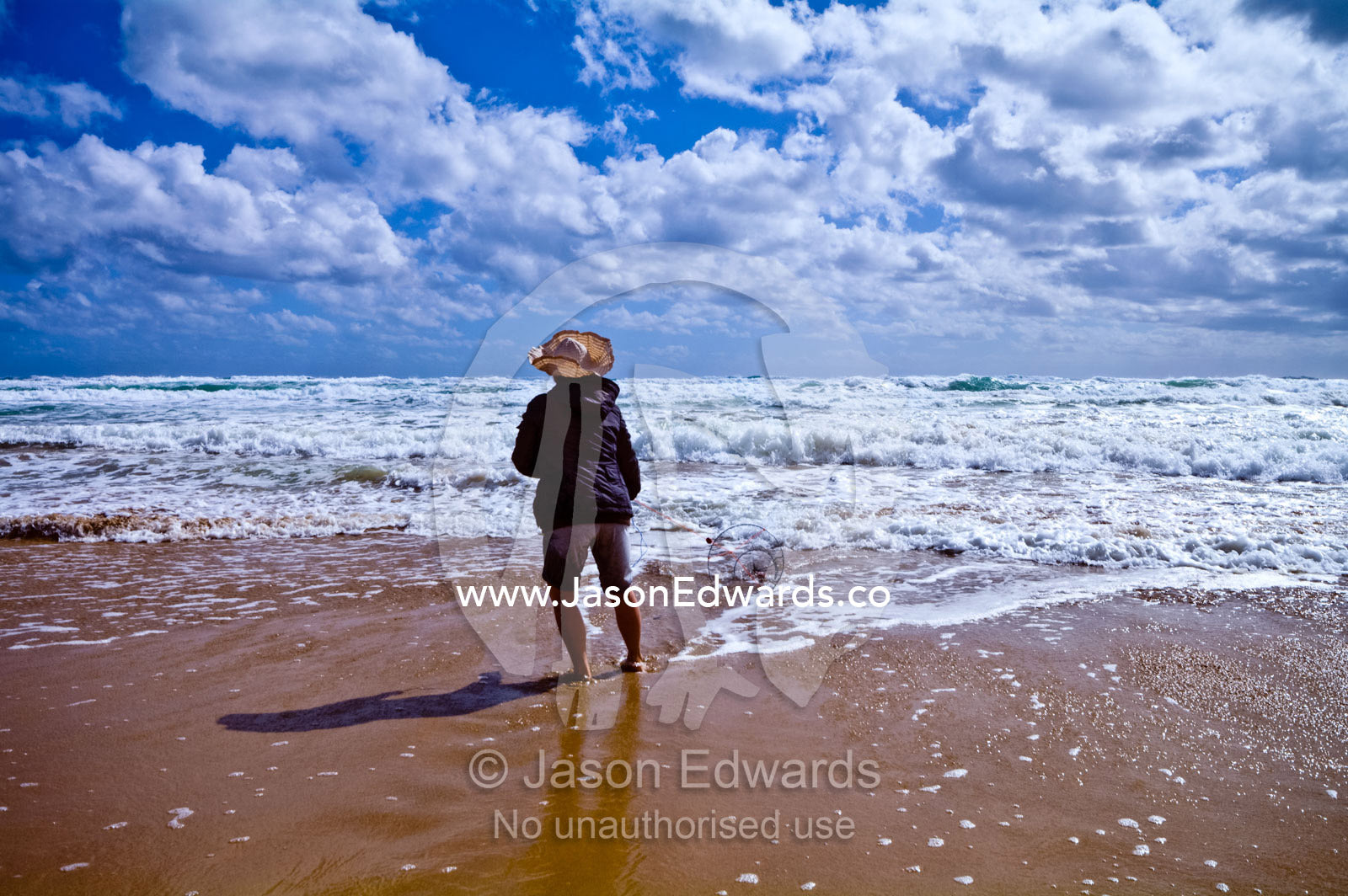 A woman fishes for pipi using a fishing line and basket in the surf. Venus Bay, Cape Liptrap Coastal Park, Bass Strait, South Gippsland, Victoria, Australia.