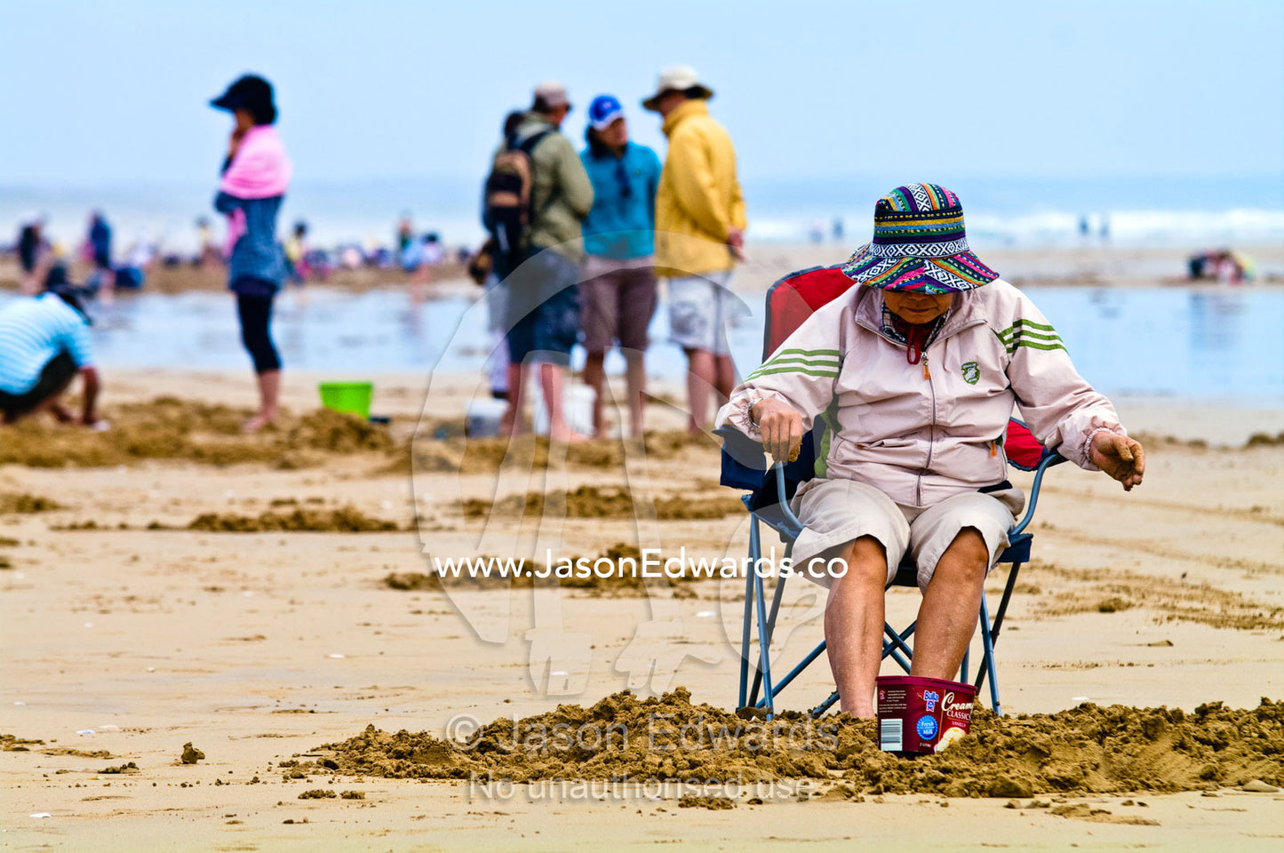 An elderly woman sleeps in a beach chair surrounded by pipi fishermen. Venus Bay, Cape Liptrap Coastal Park, Bass Strait, South Gippsland, Victoria, Australia.