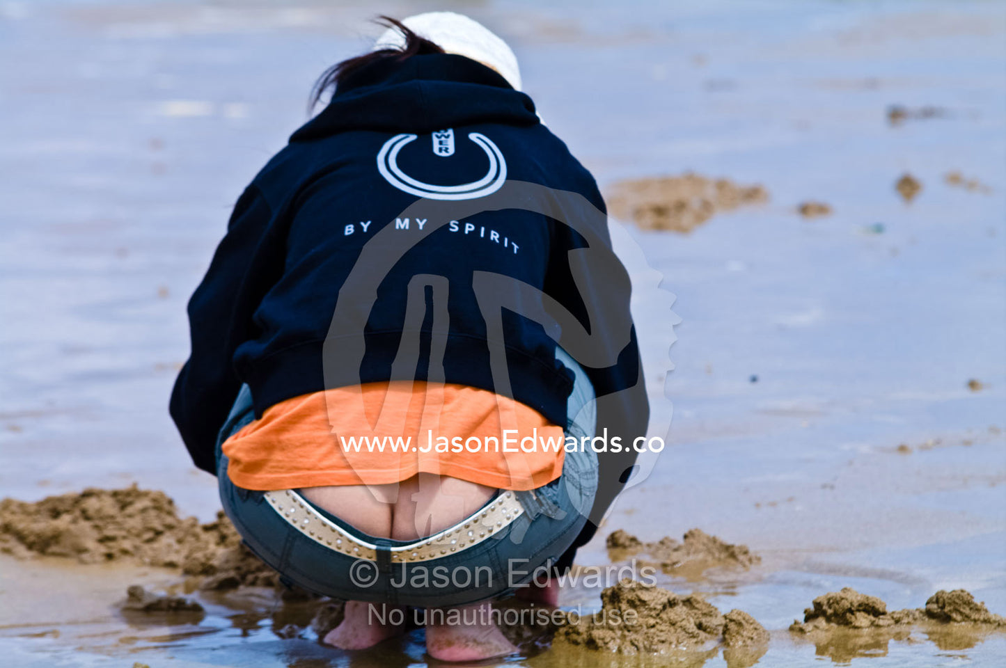 A woman digs in the sand to collect pipi from the beach at low tide. Venus Bay, Cape Liptrap Coastal Park, Bass Strait, South Gippsland, Victoria, Australia.