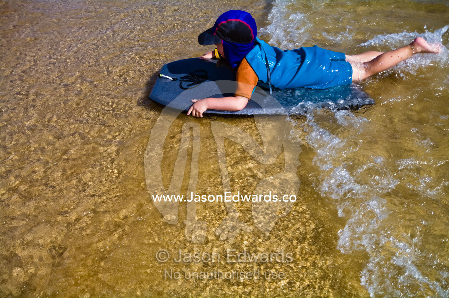 A young boy rides a body board on waves in the shallows at the beach. Venus Bay, Cape Liptrap Coastal Park, Bass Strait, South Gippsland, Victoria, Australia.