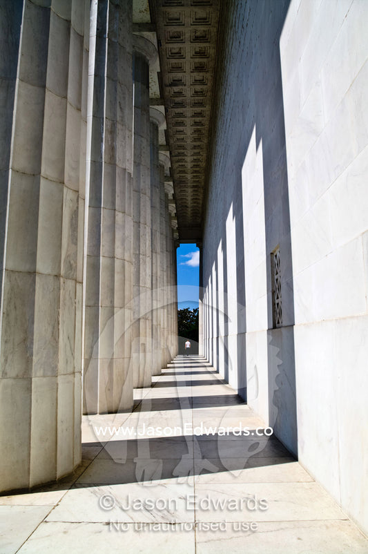 A tourist walks between marble Doric columns at the Lincoln Memorial. Lincoln Memorial, National Mall, Washington, District of Columbia, United States of America.
