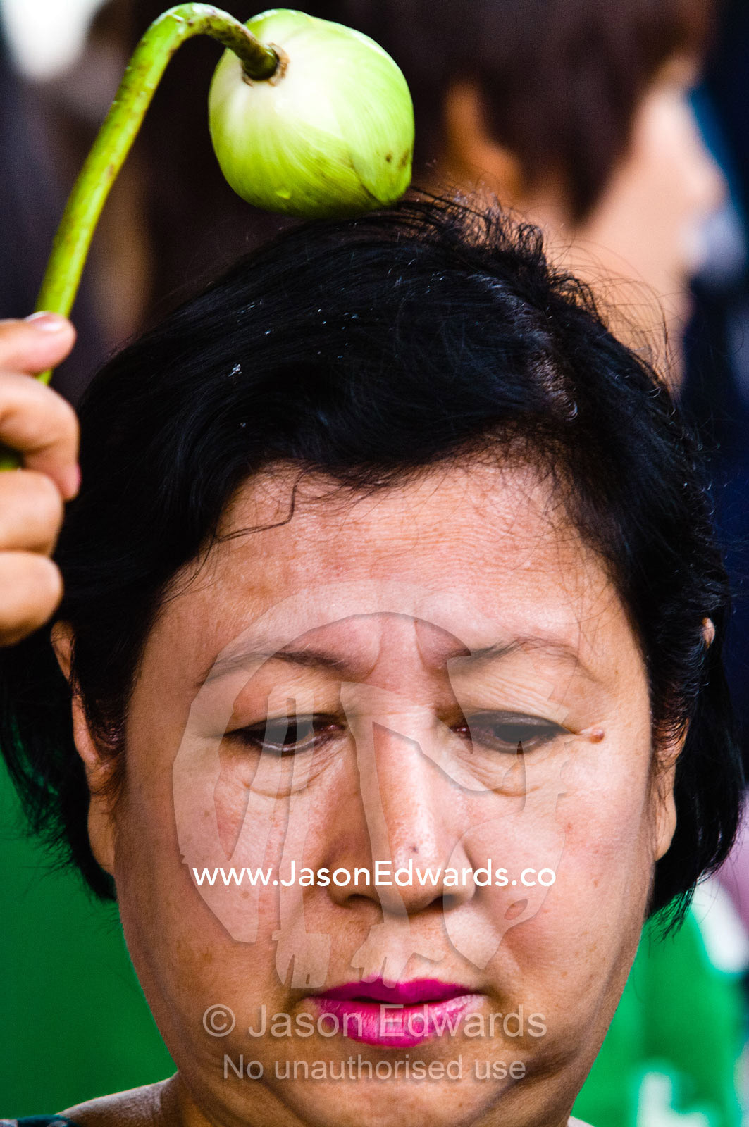 A worshipper says a prayer and touches her head with a flower bulb. Wat Phra Kaew, Wat Phra Kaeo, Temple of the Emerald Buddha, Bangkok, Thailand.