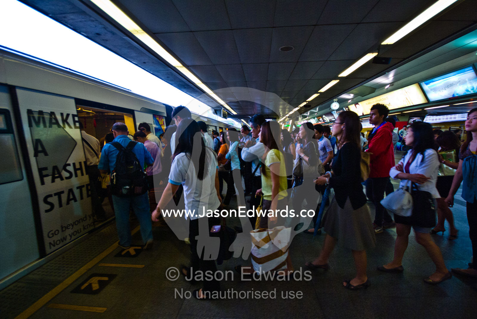 Rush hour commuters board a train from a crowded station platform. Bangkok, Thailand.
