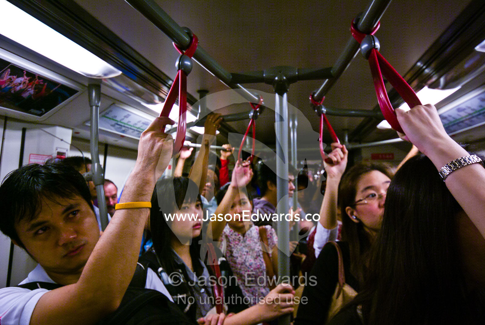 Rush hour commuters watch television to pass the time on a train. Bangkok, Thailand.