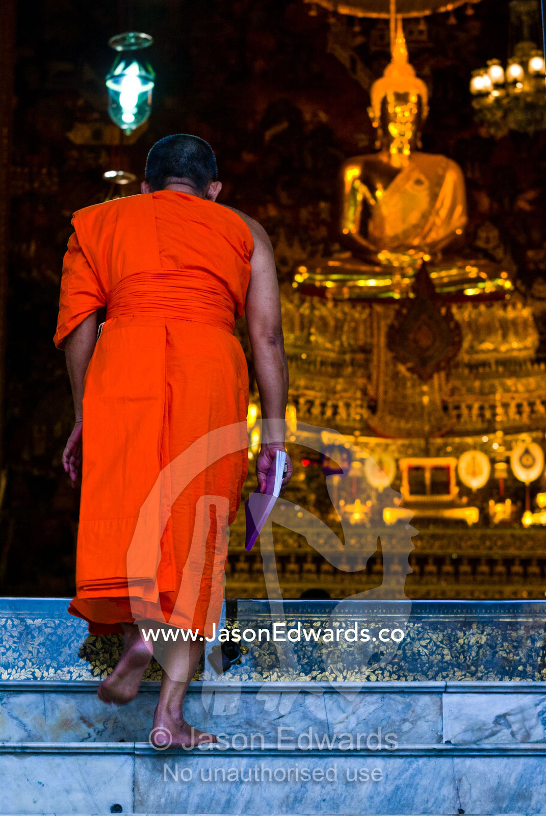 A Buddhist Monk enters a chapel beneath a golden Buddha for prayer. Wat Pho, Temple of the Reclining Buddha, Wat Chetuphon, Phra Nakhon District, Rattanakosin District, Bangkok, Thailand.