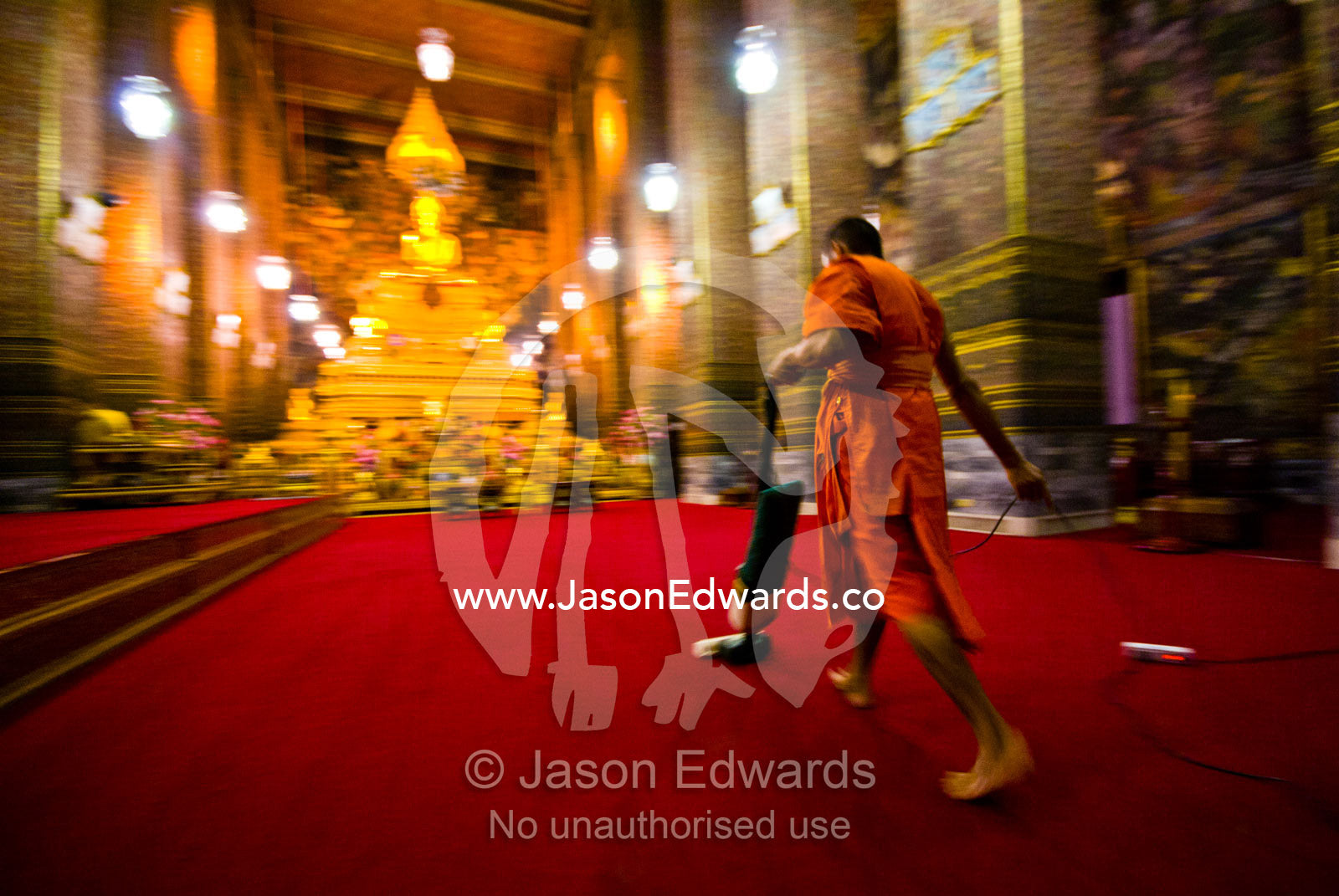 A Buddhist Monk vacuums the chapel's red carpet after evening prayer. Wat Pho, Temple of the Reclining Buddha, Wat Chetuphon, Phra Nakhon District, Rattanakosin District, Bangkok, Thailand.